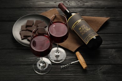 Photo of Composition with tasty red wine and chocolate on black wooden table