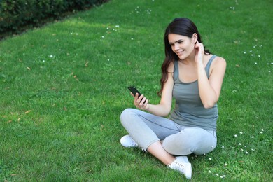 Young woman using smartphone on green grass outdoors