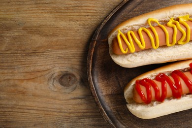 Delicious hot dogs with mustard and ketchup on wooden table, top view. Space for text