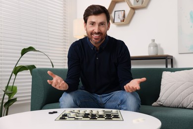Happy man inviting to play checkers at home
