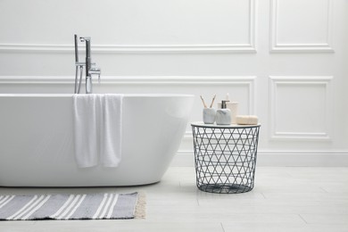 Photo of Modern ceramic bathtub and table with toiletries near white wall indoors