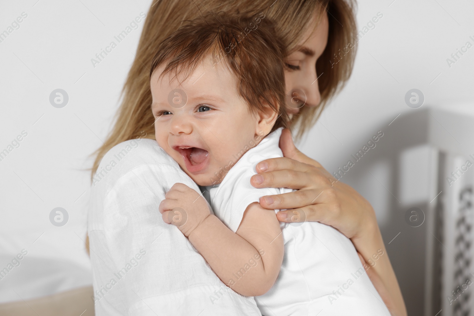 Photo of Mother hugging her cute little baby indoors, closeup