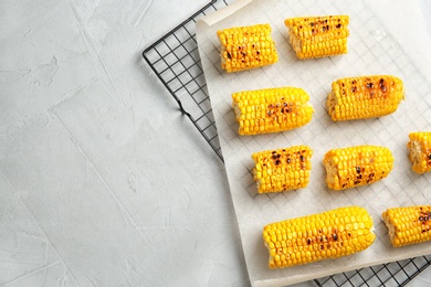 Photo of Cooling rack with grilled corn cobs on light background, top view. Space for text