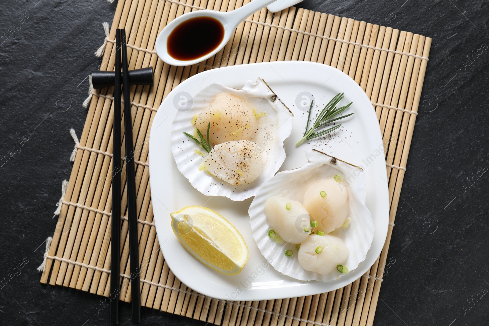 Photo of Raw scallops with green onion, rosemary, lemon and soy sauce on dark textured table, top view