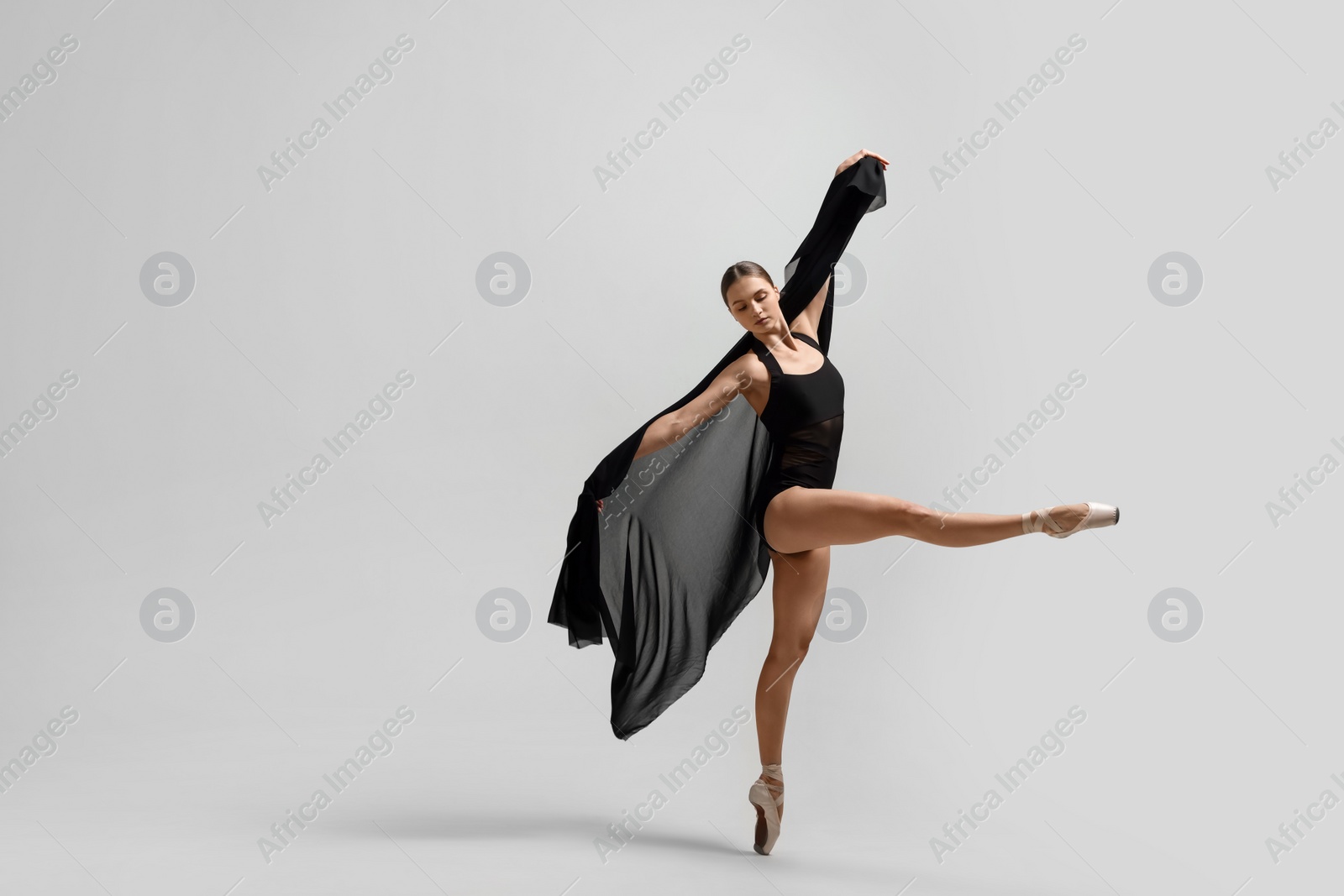 Photo of Graceful young ballerina practicing dance moves with black veil on white background