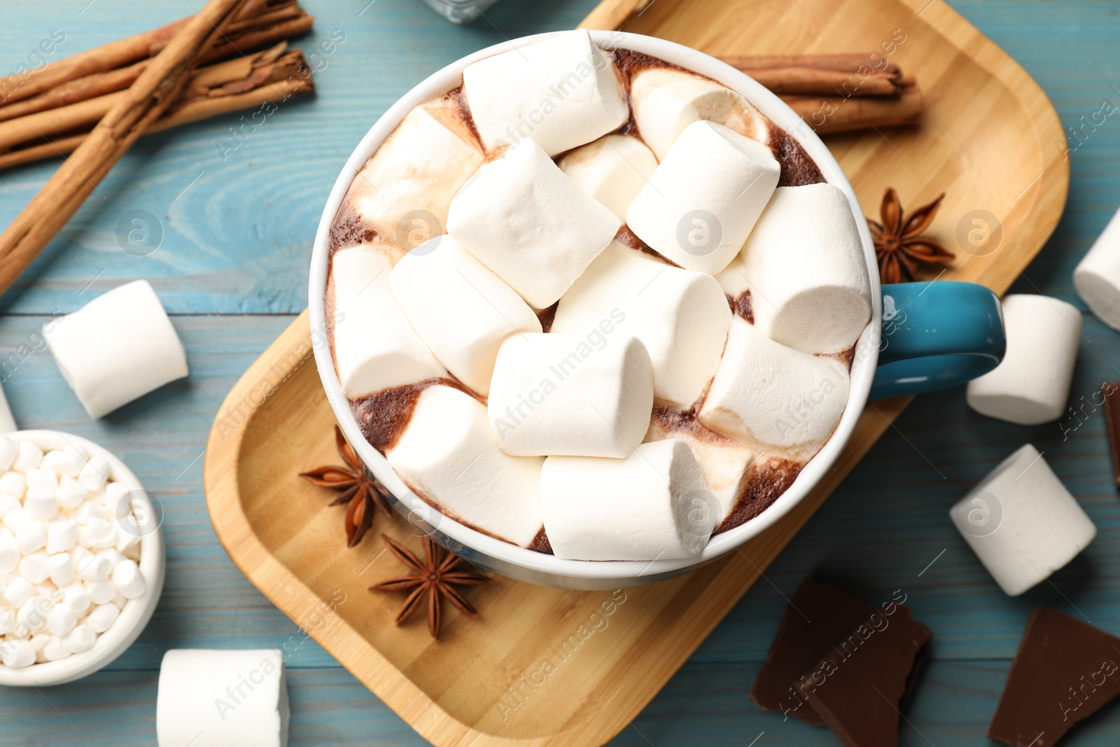 Photo of Tasty hot chocolate with marshmallows and ingredients on light blue wooden table, flat lay