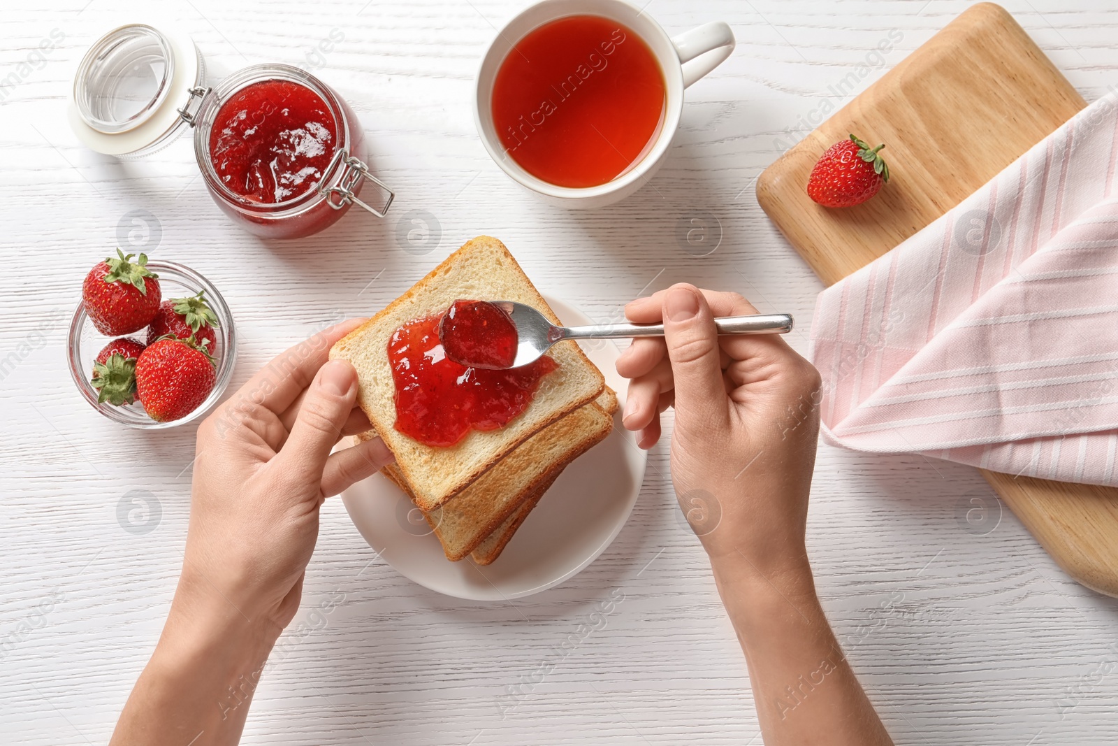 Photo of Woman spreading strawberry jam on toast bread over table