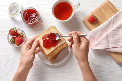 Photo of Woman spreading strawberry jam on toast bread over table