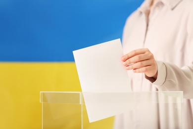 Photo of Woman putting vote into ballot box against Ukrainian flag, closeup. Space for text