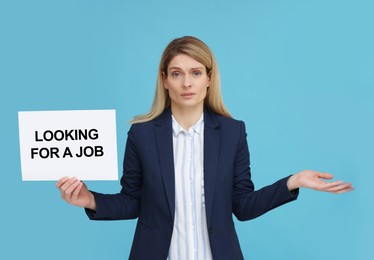 Photo of Unemployed woman holding sign with phrase Looking For A Job on light blue background