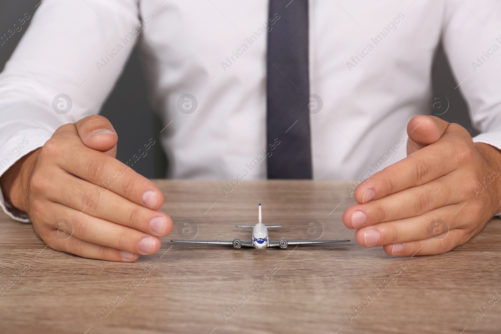 Photo of Insurance agent covering toy plane at table, closeup. Travel safety concept