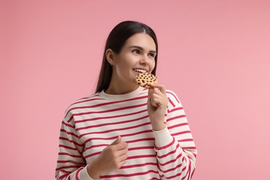 Photo of Young woman with chocolate chip cookie on pink background