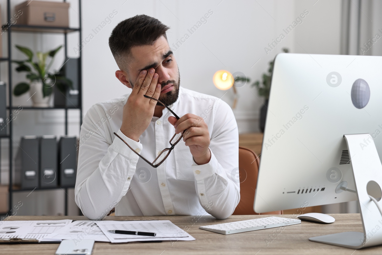 Photo of Overwhelmed man with glasses sitting at table in office