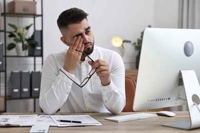 Overwhelmed man with glasses sitting at table in office