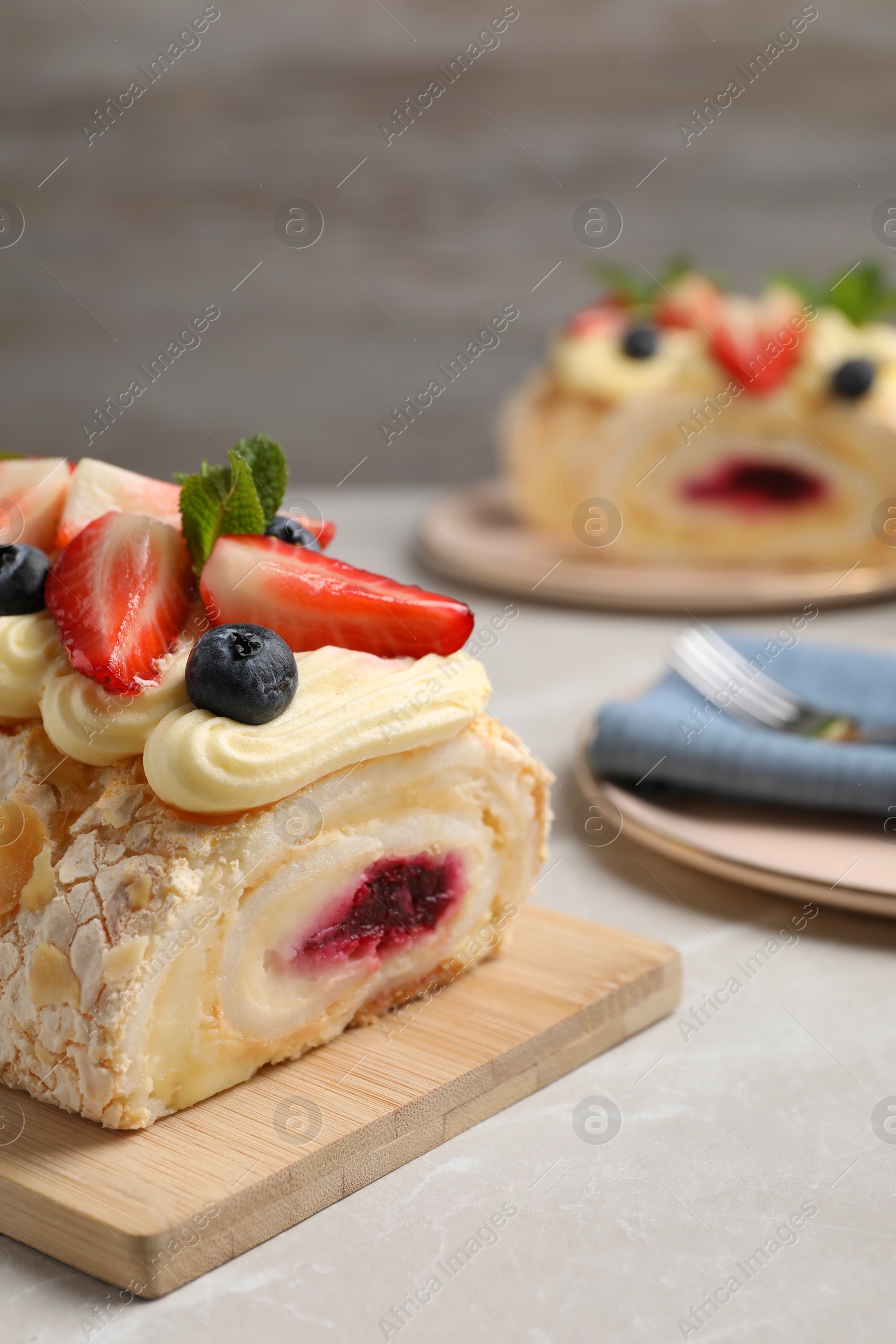 Photo of Tasty meringue roll with jam, cream, strawberry, blueberry and mint on light grey marble table, closeup