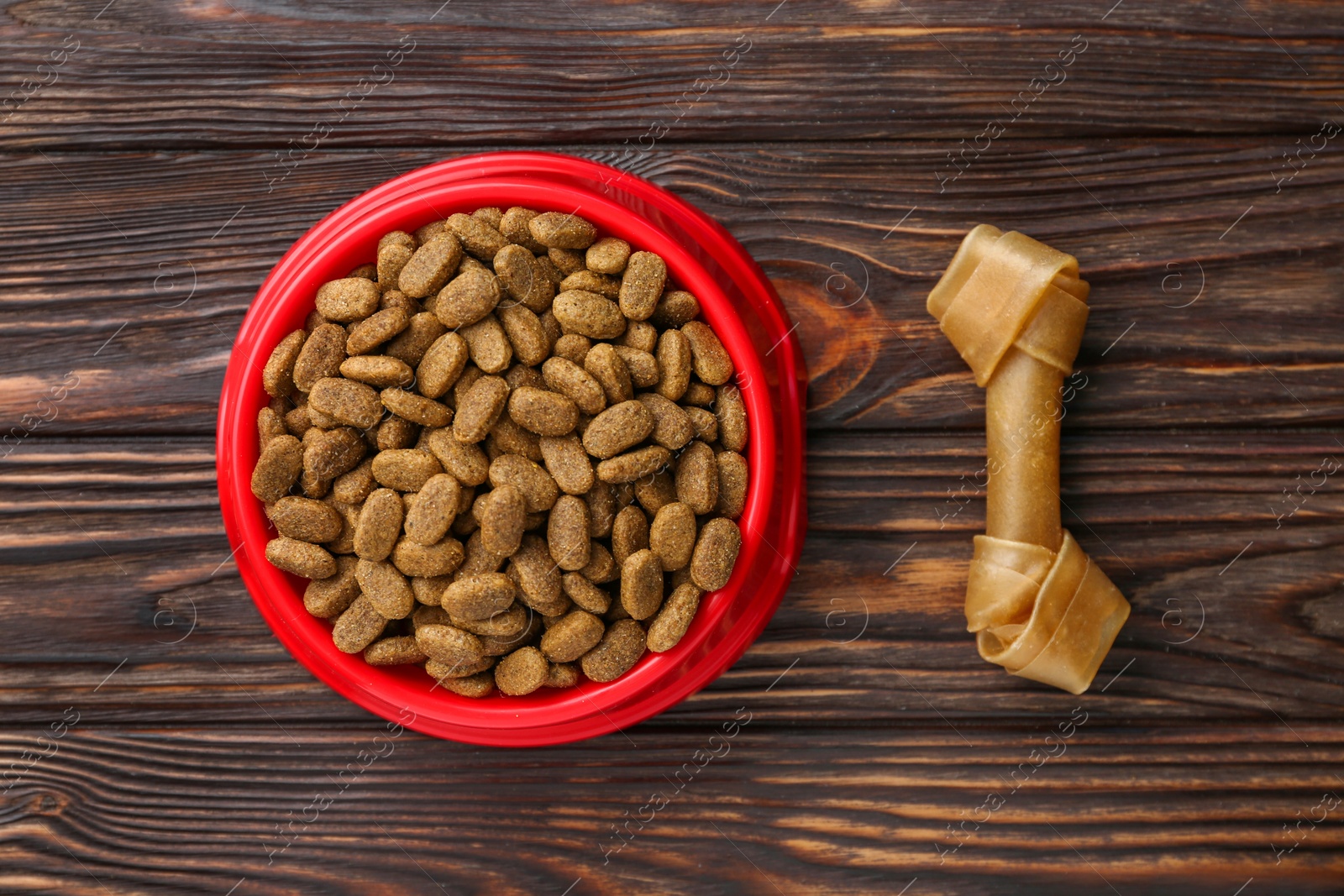 Photo of Dry dog food and treat (chew bone) on wooden floor, flat lay