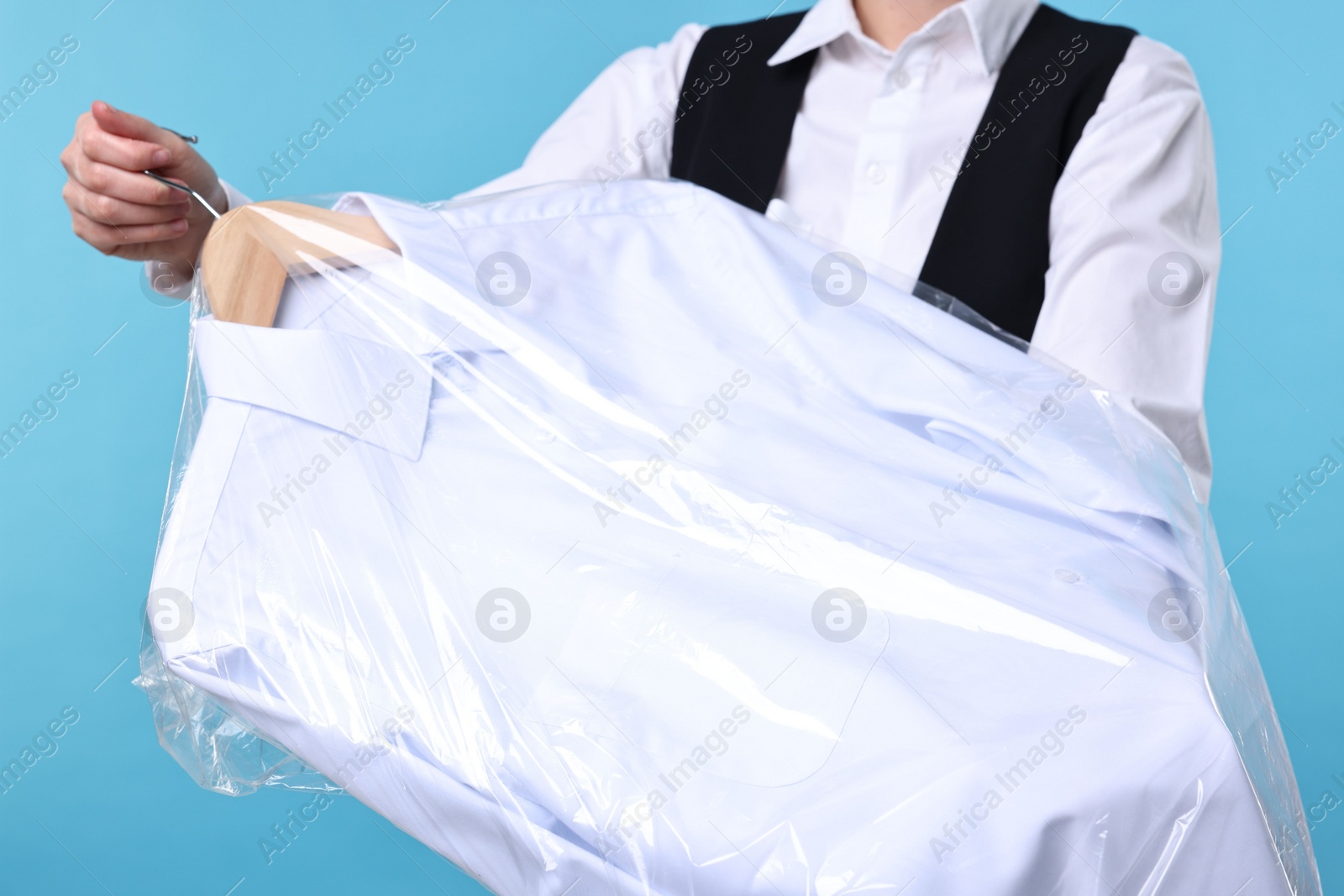 Photo of Dry-cleaning service. Woman holding shirt in plastic bag on light blue background, closeup