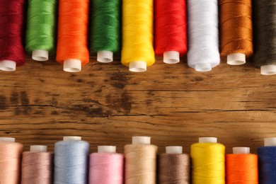 Different colorful sewing threads on wooden background, flat lay. Space for text