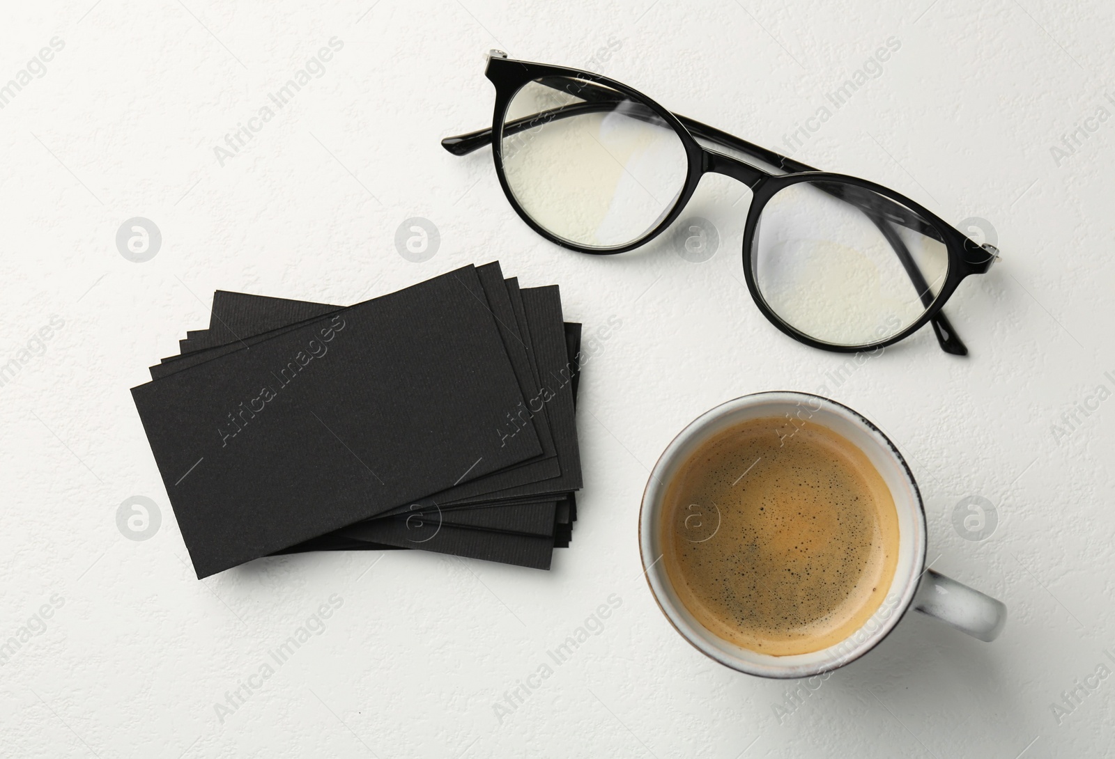 Photo of Blank black business cards, glasses and cup of coffee on white table, flat lay. Mockup for design