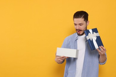Emotional man opening gift on orange background. Space for text