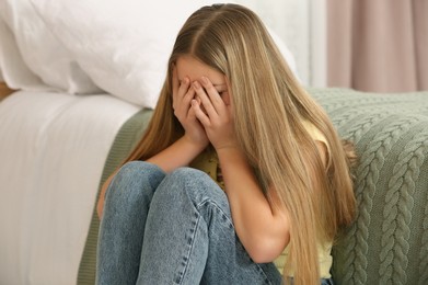 Unhappy teenage girl covering face with hands at home