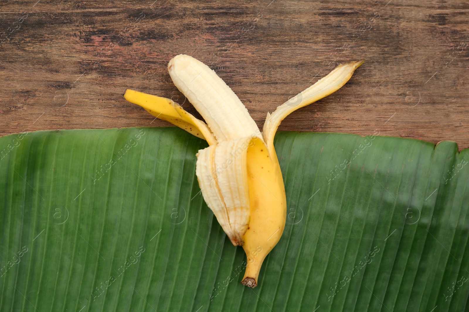 Photo of One delicious banana and fresh leaf on wooden table, top view