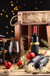 Photo of Bottles of wine, glass, wooden boxes, corks and red Christmas balls on table