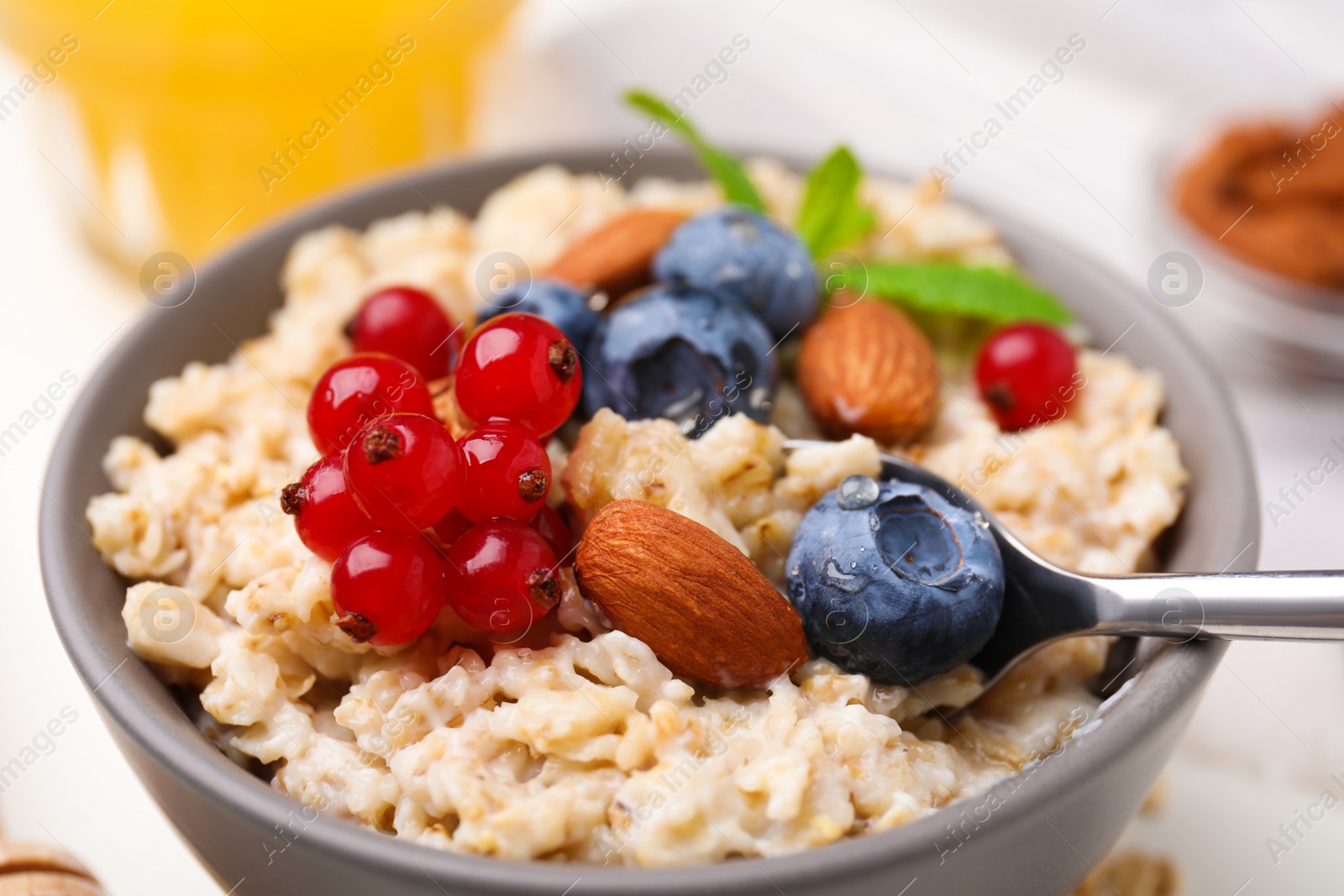 Photo of Oatmeal served with berries. almonds and mint on white table, closeup