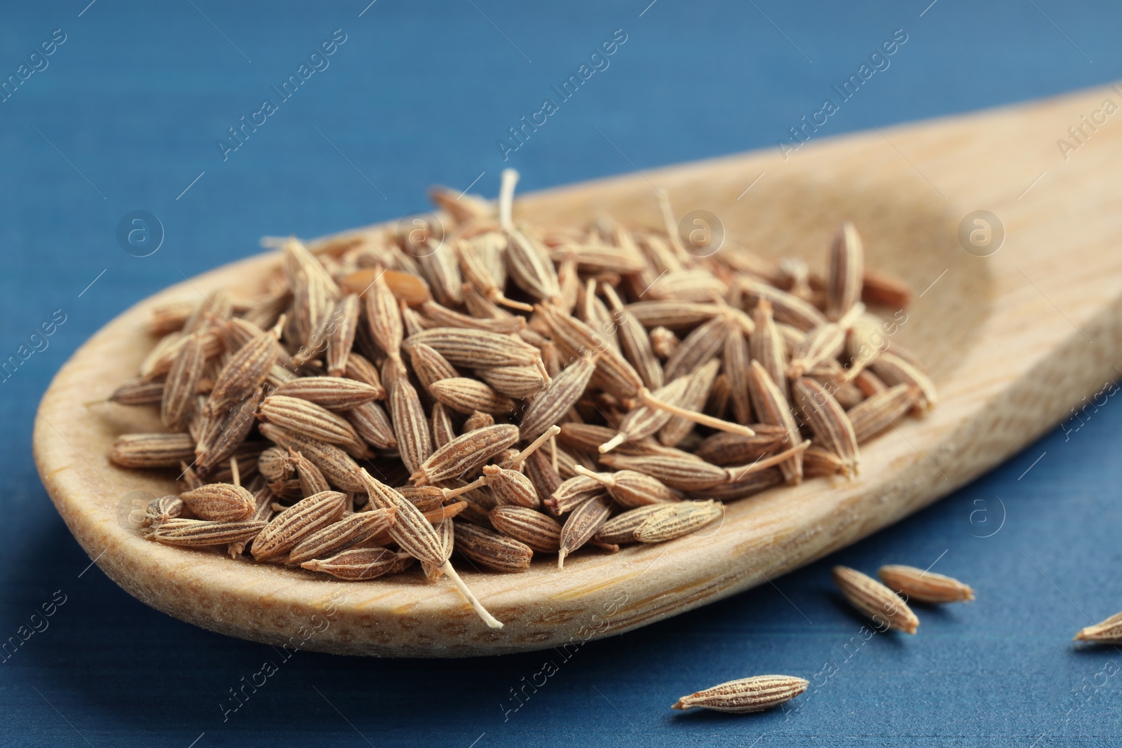 Photo of Spoon with caraway seeds on blue wooden table, closeup