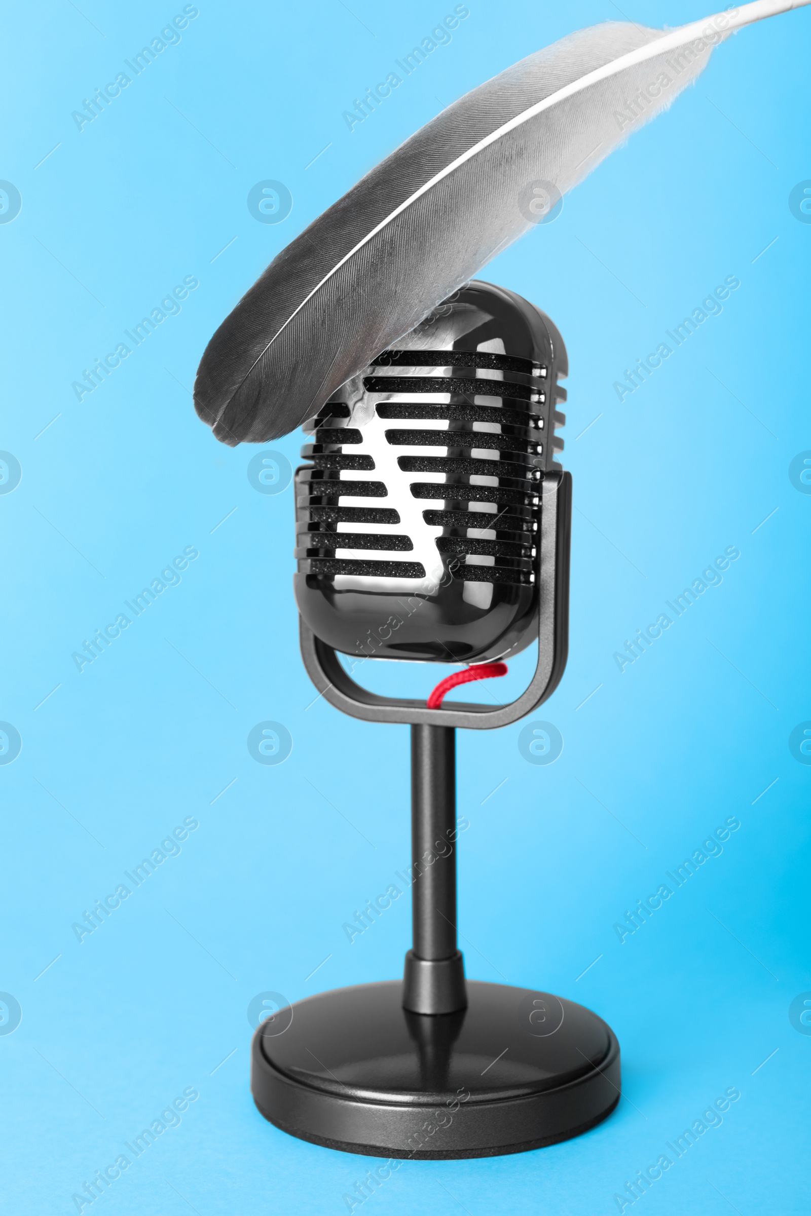 Photo of Making ASMR sounds with microphone and feather on light blue background