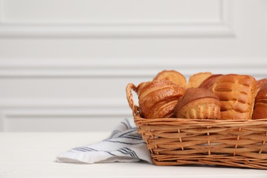 Wicker basket with different tasty freshly baked pastries on white wooden table, closeup. Space for text