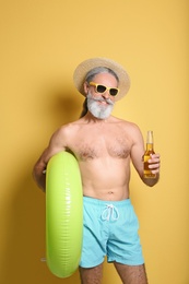 Shirtless man with inflatable ring and bottle of drink on color background