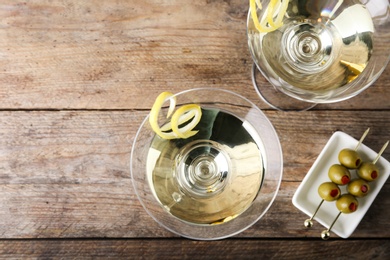 Photo of Glasses of lemon drop martini cocktail with zest on wooden table, flat lay