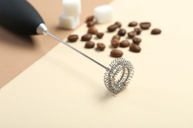 Milk frother wand, coffee beans and sugar cubes on color background, closeup