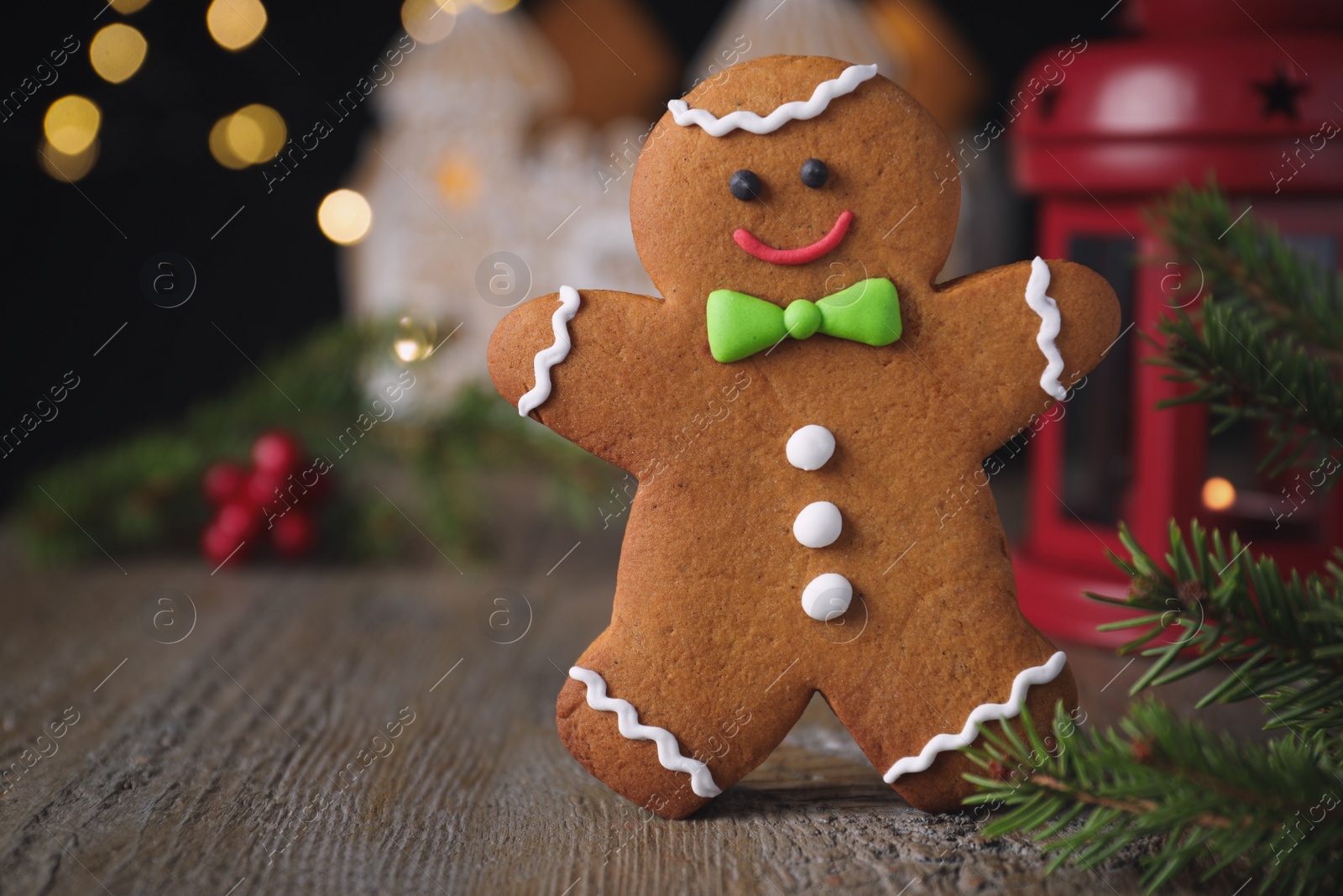 Photo of Gingerbread man on wooden table against blurred lights, closeup. Space for text