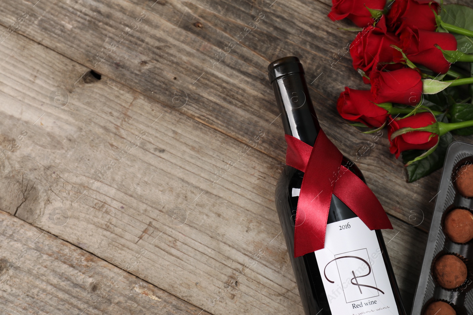 Photo of Bottle of red wine, chocolate truffles and roses on wooden table, flat lay. Space for text