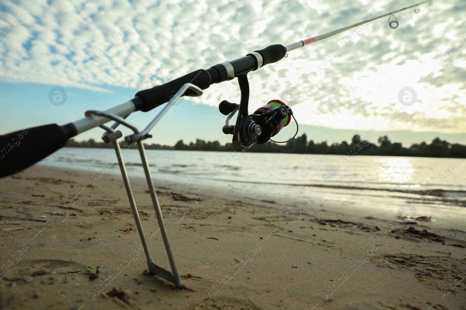 Photo of Fishing rod with reel on sand near river, space for text