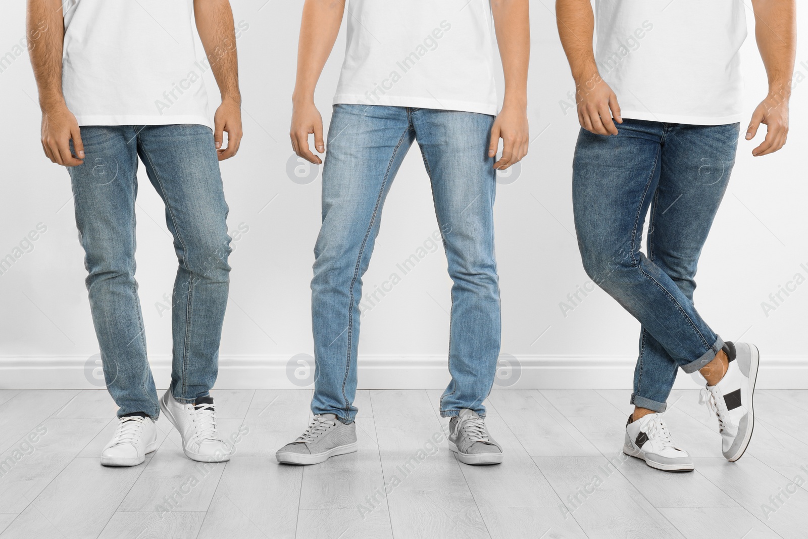 Photo of Group of young men in stylish jeans near white wall, closeup