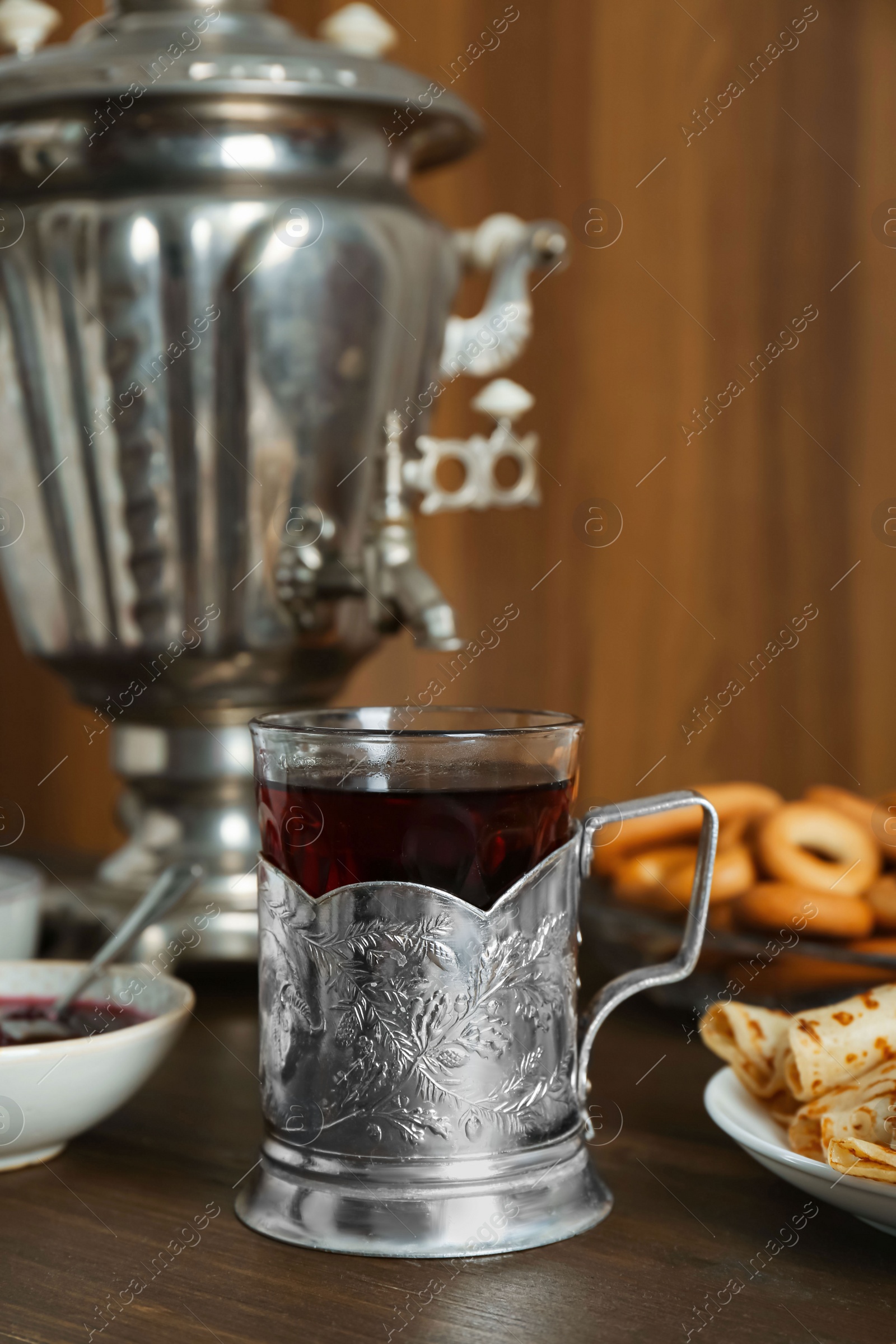 Photo of Vintage samovar, cup of hot drink and snacks served on wooden table. Traditional Russian tea ceremony