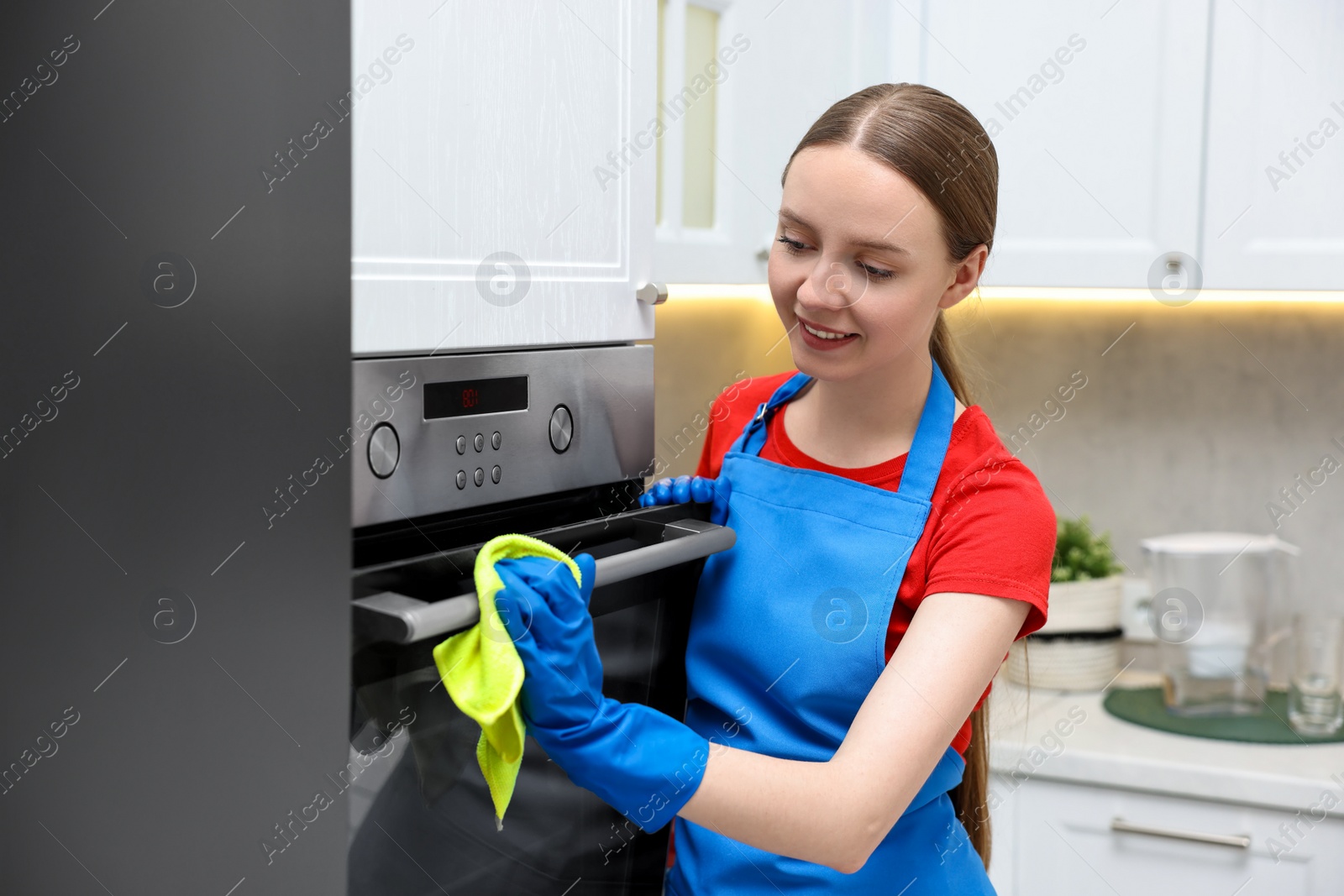 Photo of Woman cleaning electric oven with rag in kitchen