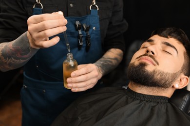 Photo of Hairdresser with beard oil near client in barbershop, closeup. Professional shaving service
