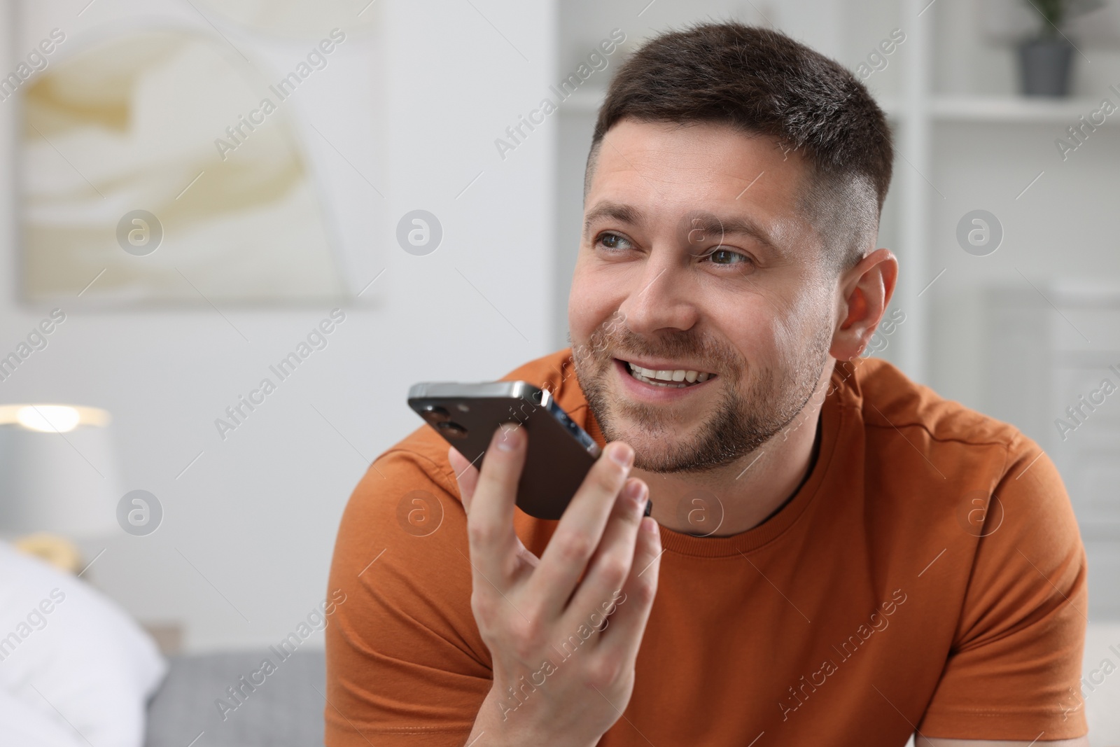 Photo of Handsome man recording voice message via smartphone at home