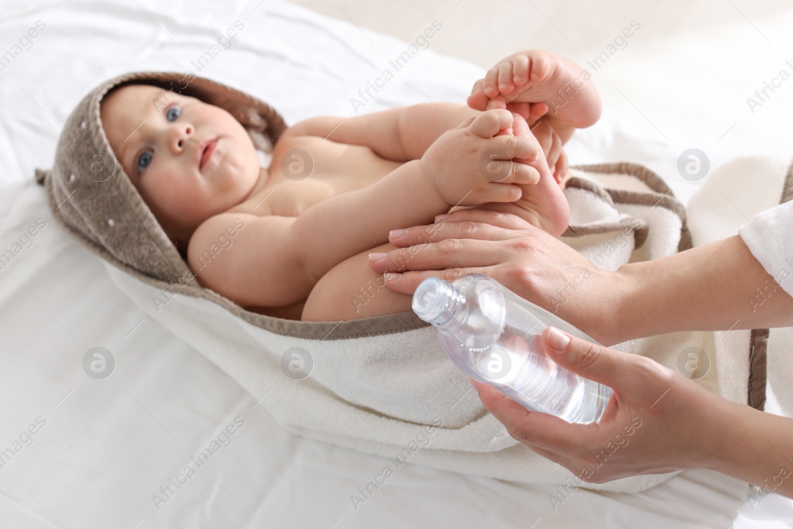 Photo of Mother massaging her cute baby with oil on bed, closeup