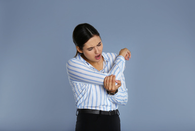 Image of Young woman suffering from elbow pain on grey background