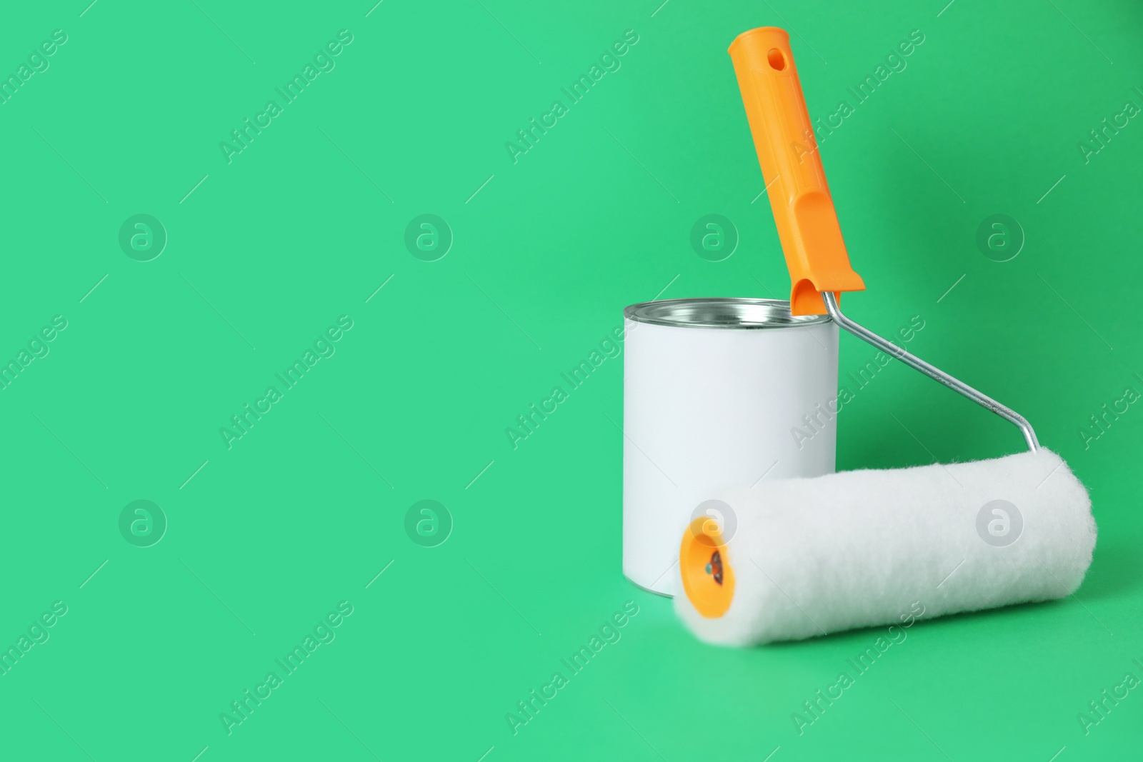 Photo of Can of orange paint and roller brush on green background. Space for text