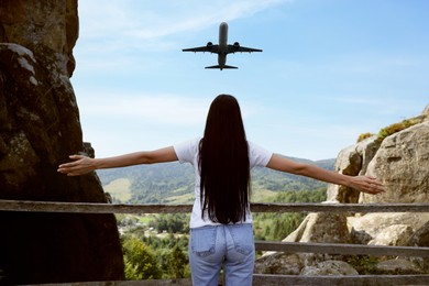 Woman looking at airplane flying in sky over mountains, back view