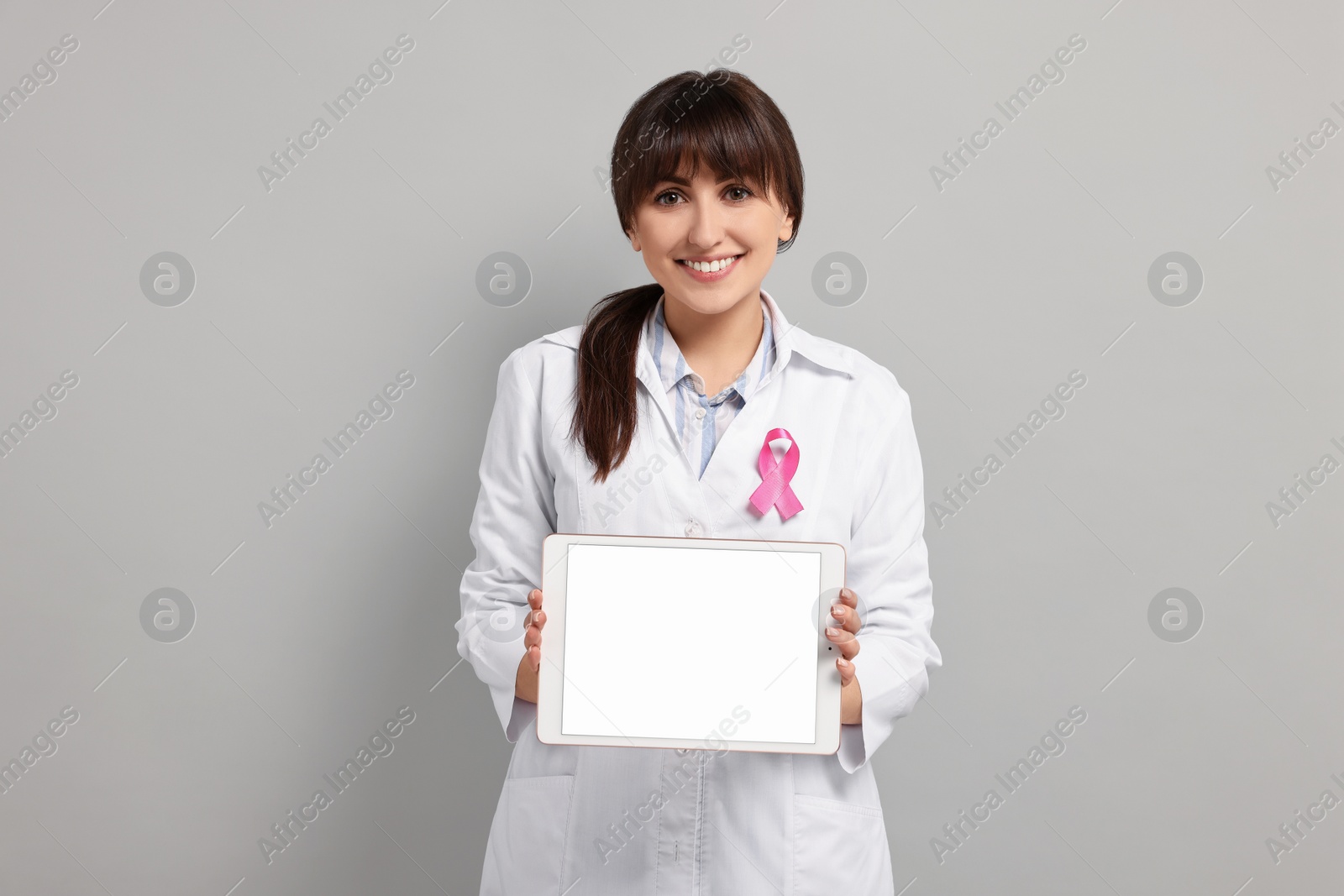 Photo of Mammologist with pink ribbon showing tablet on light grey background. Breast cancer awareness