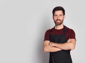 Professional hairdresser wearing apron with on light grey background, space for text