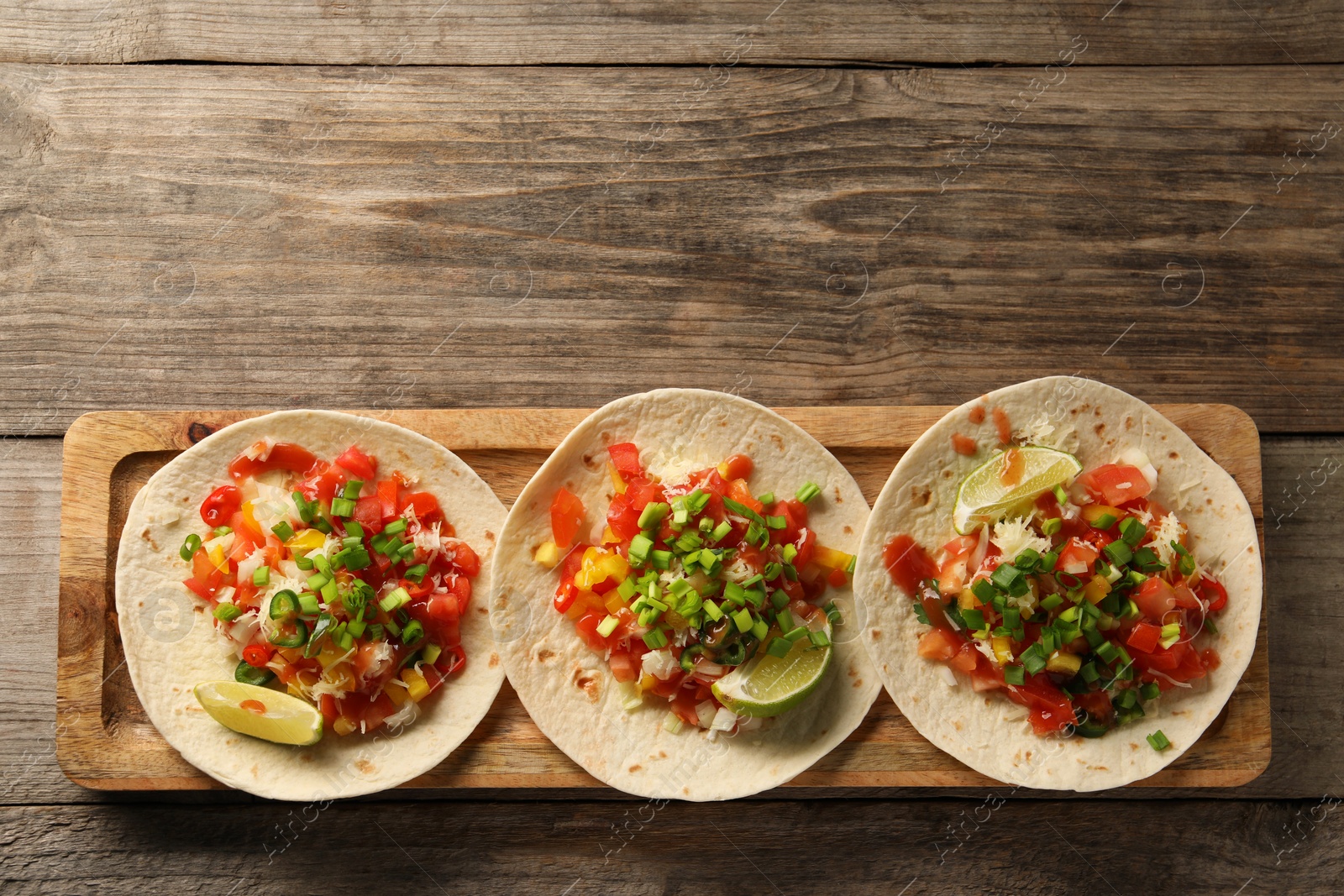 Photo of Delicious tacos with vegetables, green onion, lime and ketchup on wooden table, top view. Space for text