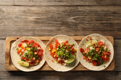 Photo of Delicious tacos with vegetables, green onion, lime and ketchup on wooden table, top view. Space for text